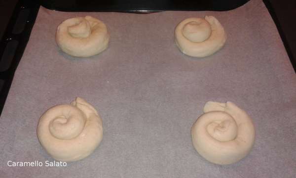 Formare con ogni parte un rotolo lungo 35 cm. ed arrotolarlo a chiocciola, disporre le il pane a chiocciola sulla placca del forno 