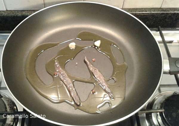 In una pentola capiente versare l'olio, lo spicchio di aglio, i filetti d'acciuga ed il peperoncino, far sciogliere le acciughe 